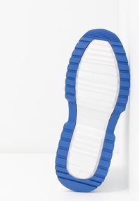 Blå gummisul med djupa spår och en vit mellansula; har präglat varumärkesnamn. Slät yta med en flexibel design.