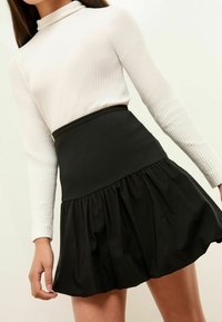 Haut blanc à manches longues en maille côtelée avec un col montant ; jupe noire évasée avec une taille lisse et un tissu texturé.