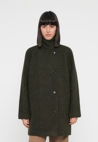 Olive green wool coat with a high collar, oversized fit, and black buttons. Features long sleeves and a soft, textured finish.
