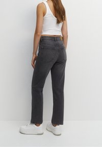 Jean gris taille haute avec jambes droites, comportant deux poches arrière et une étiquette en cuir de marque sur la taille, portés avec des baskets blanches.