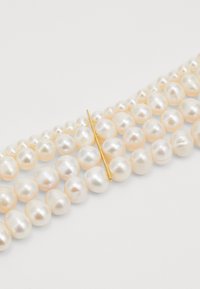 Perlenarmband mit unregelmäßig geformten, schimmernden weißen Perlen mit einem subtilen Glanz, akzentuiert durch eine goldfarbene Nadel.
