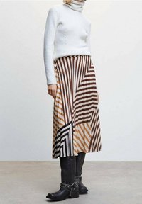 Jupe midi rayée en marron, crème et noir, avec des motifs géométriques. Assortie à un pull col roulé côtelé blanc et des bottes noires.