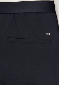 Pantaloni blu navy con una tasca posteriore, texture liscia e un piccolo logo. Design semplice, vestibilità standard e cinturino elastico.