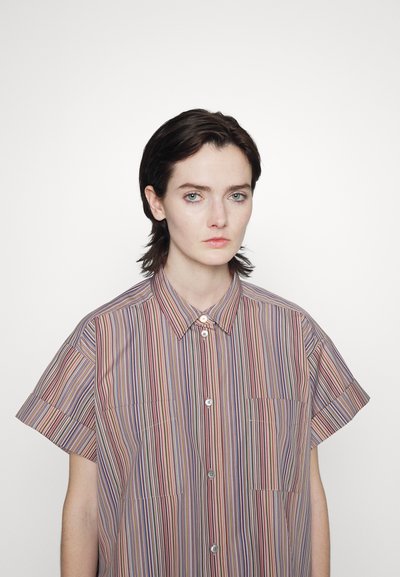 Camisa de botão de manga curta com riscas verticais em vermelho, azul e creme. Dois bolsos frontais e colarinho clássico. Textura de algodão.