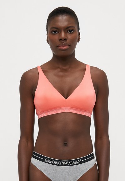 Peach wireless bralette with a V-neck design, smooth texture, and a logo band under the bust. Paired with gray briefs featuring a black waistband.