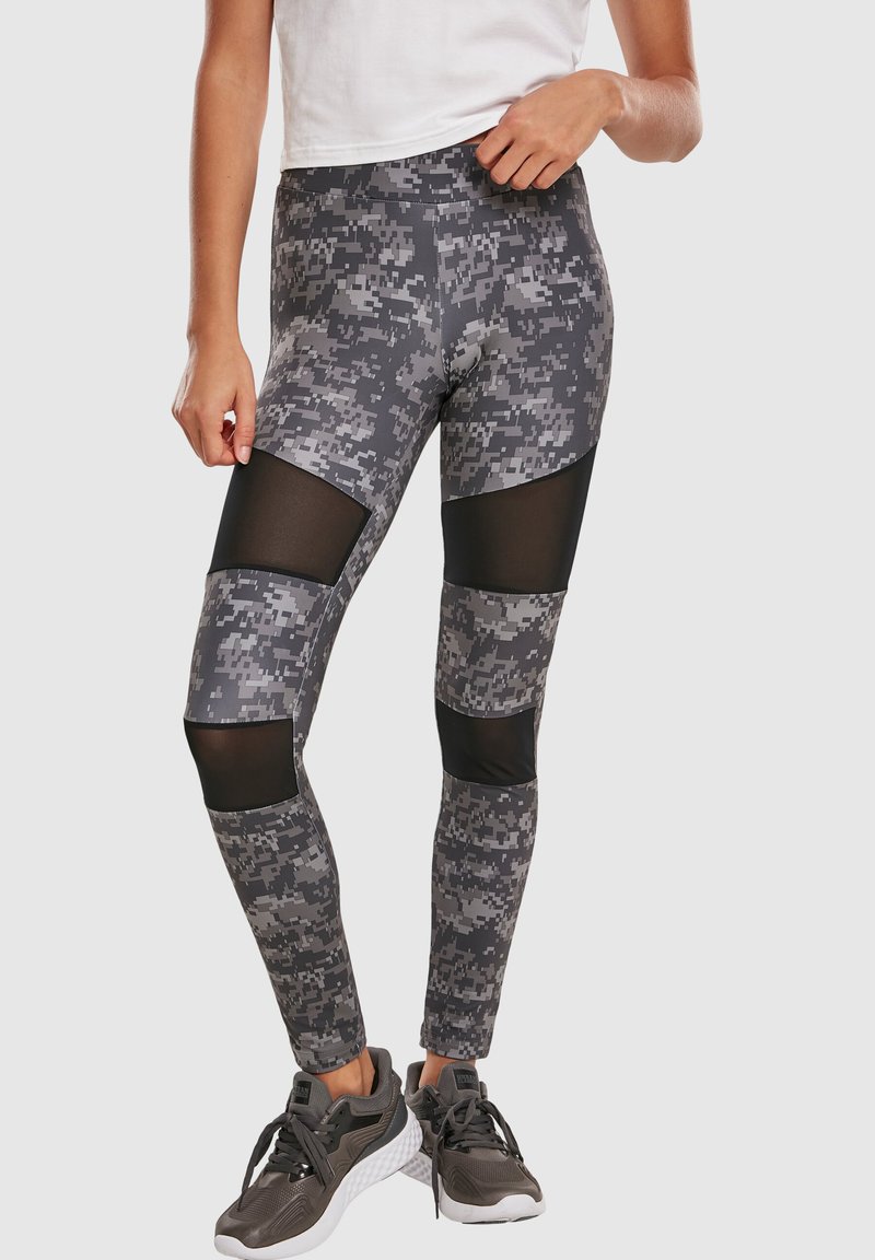 Grå camo leggings med meshpaneler ved knæene, tætsiddende design, høj talje og tekstureret stofdetalje. Kombinert med grå træningssko.