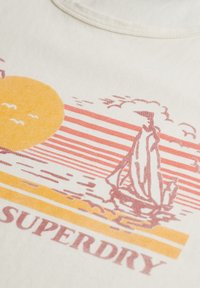Camiseta de algodón en color crema con un gráfico de estilo vintage. Presenta un sol, un velero y el texto “SUPERDRY” en tonos de naranja y rosa.