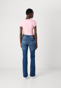 Tett rosa t-skjorte og blå slengbukser. T-skjorten har korte ermer, buksene har en baklomme og et lysebrunt skinnakcent.