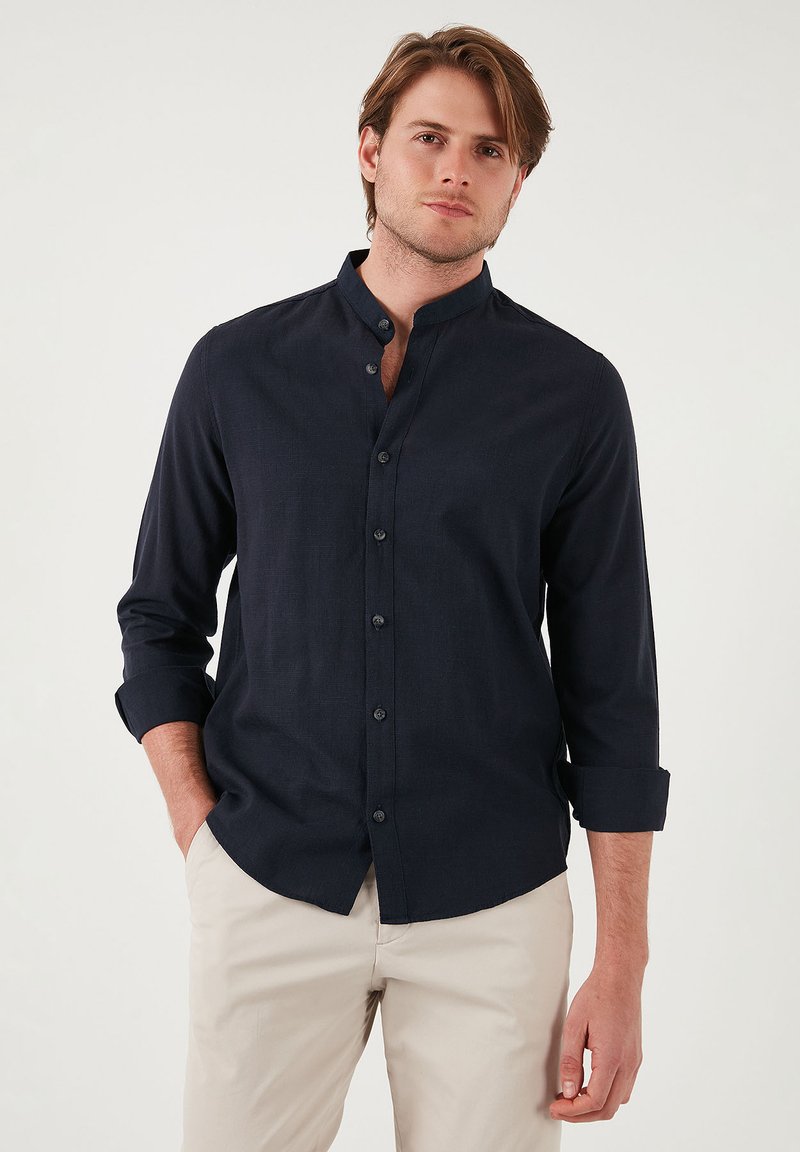 Camisa navy de botones con cuello alzado, de manga larga enrollada en los puños, confeccionada en una tela texturizada. Presenta cinco botones en la parte delantera.