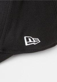 Gorra de béisbol negra con un logotipo bordado en blanco en la parte frontal. El material es tela texturizada con un visera curva y detalles cosidos.