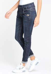 Mörkblå slim-fit jeans med synlig sömnad, framfickor och uppvikt fåll. Bärs med vita sportskor.