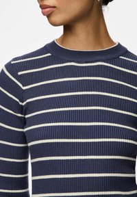 Granatowy sweter prążkowany z białymi poziomymi paskami. Posiada okrągły dekolt oraz dopasowany krój. Gładka tekstura, średniej wagi materiał.