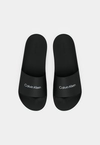 Infradito neri con una fascia larga che presenta il testo bianco "Calvin Klein". Realizzati in materiale liscio con suola piatta.