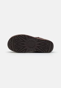 Semelle de botte brun foncé avec des motifs de bande de roulement angulaires et circulaires pour une meilleure traction, présentée sur un fond clair uni.