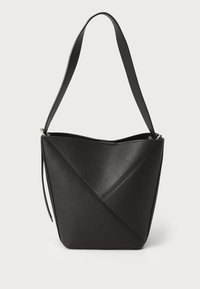 Melna ādas spainīša soma ar diognālu šuvju dizainu, vienu plecu siksnu un atvērtu augšu, kas izceļ gludu tekstūru.