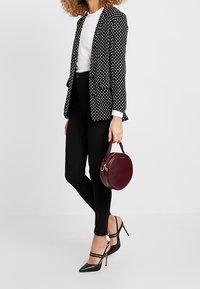 Czarna marynarka w białe kropki, biały top i czarne jeansy. Czarne buty na obcasie z zaostrzonym noskiem oraz okrągła bordowa torebka z uchwytem.