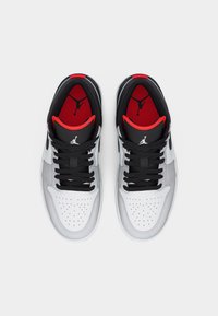 Ζευγάρι λευκά, γκρι και μαύρα αθλητικά παπούτσια Air Jordan με κόκκινη εσωτερική επένδυση και μαύρα κορδόνια, φωτογραφημένα από πάνω πάνω σε λευκό φόντο.