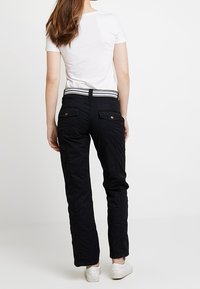 Zwarte broek met een rechte pasvorm, zakdetails en een gestreepte tailleband. Gecombineerd met een eenvoudig wit T-shirt en witte sneakers.