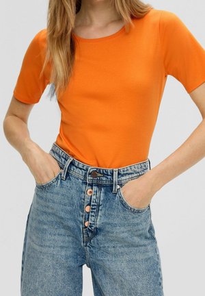 Pomarańczowa koszulka z krótkim rękawem z bawełny, w zestawieniu z jasnoniebieskimi dżinsami o wysokim stanie z zapięciem na guziki i bocznymi kieszeniami.