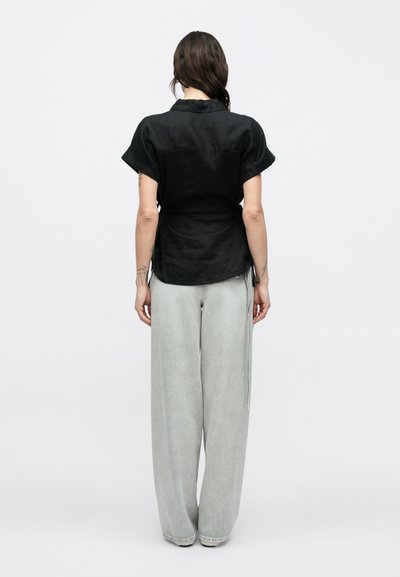 Μαύρο λινό πουκάμισο με κοντά μανίκια και στρογγυλεμένο γιακά, συνδυασμένο με ανοιχτό γκρι τζιν παντελόνι φαρδύ με διακριτική υφή και λεπτομέρειες στην πλαϊνή ραφή.