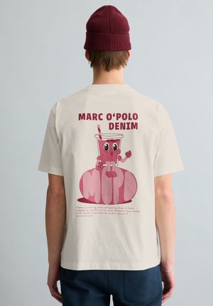 Personne portant un t-shirt crème avec un personnage de smoothie à la framboise en dessin animé et le texte "MARC O'POLO DENIM" au dos, assorti d'un bonnet bordeaux.