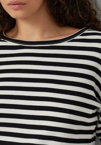Schwarz-weiß gestreiftes Oberteil mit gerippter Textur, weiter Halslinie und lockerer Passform. Die Streifen wechseln sich in breiten und schmalen Breiten ab.