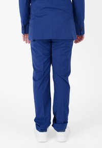 Abito blu su misura con un'unica apertura e una texture liscia, abbinato a scarpe da ginnastica bianche. Cuciture visibili e dettagli con bottoni sulle maniche.