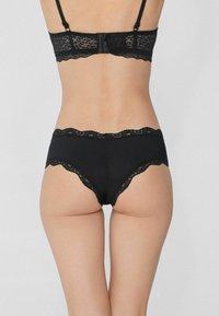 Czarny komplet bielizny z koronkowym wykończeniem: biustonosz i majtki. Miękka tkanina z misternymi akcentami koronkowymi, z falbaniastym brzegiem i regulowanymi ramiączkami.