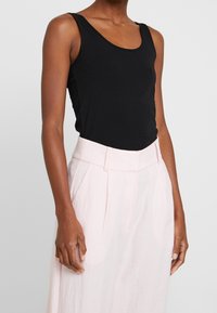 Musta ilmanhiha tank top pehmeästä kankaasta, yhdistettynä korkeavyötäröisiin vaaleanpunaisiin housuihin, jotka esittelevät sileää pintaa ja muotoiltua istuvuutta.