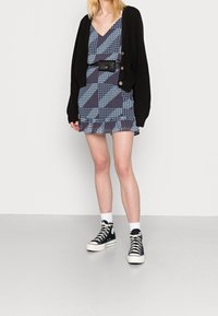 Svart stickad cardigan över en blåmönstrad klänning med en flippad nederkant. Tillsammans med svarta högskor och vita strumpor.