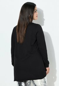 Zwarte langesleeve top met een rechte snit en lichte zijsplitten, gemaakt van zachte stof, gecombineerd met glanzende zilveren paillettenbroek.