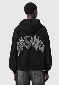 Zwarte hoodie met een oversized pasvorm, featuring zilveren "ALL SAINTS" tekst in een gejagde stijl op de achterkant. Katoenen materiaal met een zachte textuur.
