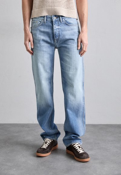 Jeans din denim de un albastru deschis, cu un design drept, textură decolorată și stil cu cinci buzunare, asortați cu adidași maronii cu șireturi albe.