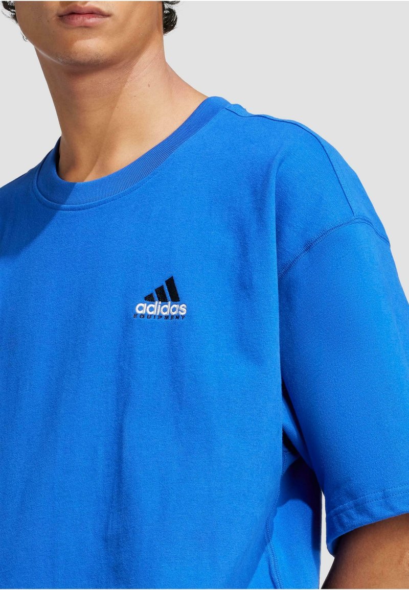 Blå bomulds T-shirt med rund halsudskæring og korte ærmer. Har et sort og hvidt broderet Adidas-logo på brystet.