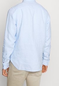 Hellblaues, langärmliges Hemd aus Leinen mit einem Button-Down-Kragen und Ein-Knopf-Manschetten. Taillierter Schnitt mit abgerundetem Saum.