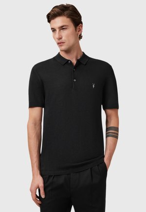 Schwarzes, kurzärmeliges Poloshirt aus weichem Stoff, mit Kragen, drei Knöpfen und einem kleinen Logo auf der Brust. Glatte Textur.