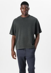 Dark gray oversized t-shirt with short sleeves, crew neckline, soft texture, and unfinished hem detail. Paired with navy pants.