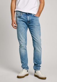 Heled sinine denim teksad sirge säärega lõikega, millel on viis taskut ja tuhmumise efekt. Kombineeritud valgete tennisetossude ja lihtsa valge T-särgiga.