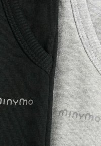 Nahaufnahme von schwarzem und grauem Stoff mit sichtbaren Nähten und teilweise sichtbarem "minymo" Markentext auf jedem Stück.