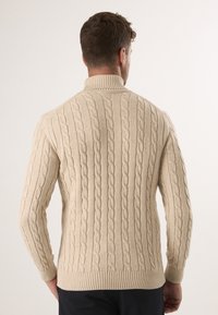 Beżowy sweter z dzianiny w sploty, z wysokim kołnierzem, z teksturowanym wzorem plecionych warkoczy oraz prążkowanymi mankietami i dołem.