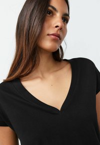 Mustast siledast puuvillast valmistatud must V-kaelusega lühikeste varrukatega pluus, millel on puhas kaelus ja peened õmblused.