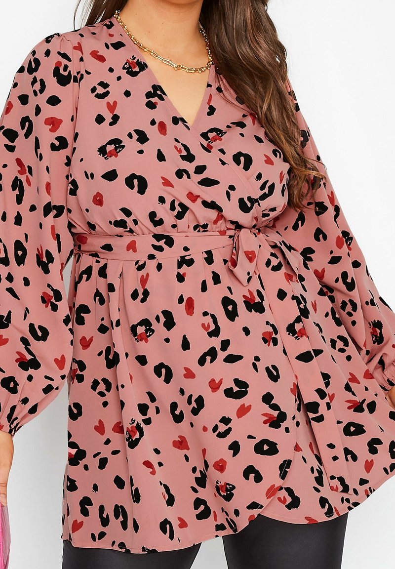 Haut cache-cœur rose avec imprimé léopard noir et rouge, manches longues bouffantes et ceinture à nouer à la taille. Tissu léger et fluide avec une texture lisse.