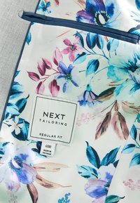 Tissu à motif floral avec des fleurs bleues, violettes et roses, comportant une étiquette "NEXT Tailoring Regular Fit" et une taille "40R Made in Vietnam."