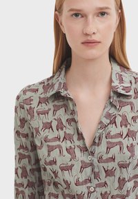 Camicia button-up verde chiaro con una stampa ripetuta di cani color bordeaux, dall'aspetto morbido e con un design di colletto classico.