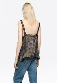 Przezroczysta brązowa bluzka w kratę z czarną koronką. Posiada ramiączka spaghetti oraz rozkloszowany krój, ozdobiona abstrakcyjnym złotym wzorem.