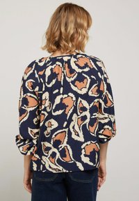 Blouse marine à imprimé floral abstrait large en beige et corail. Avec des manches ballon et un col froncé. Tissu doux et léger.
