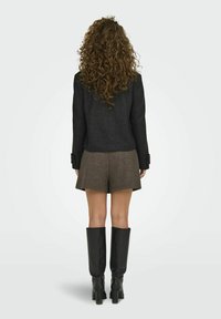 Svart ullblazer, brune mønstrede shorts, knelang svarte lærstøvler. Krøll håret synlig, fokus på klærnes design og materialer.