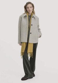 Grauer Wollmantel mit Kragen, zwei Knöpfen und Seitentaschen, kombiniert mit einem senfgelben Schal und einem olivgrünen Hemd, getragen zu dunklen Hosen.