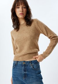 Pull en tricot marron clair à manches longues et col rond, associé à un jean en denim bleu avec un design classique à cinq poches.