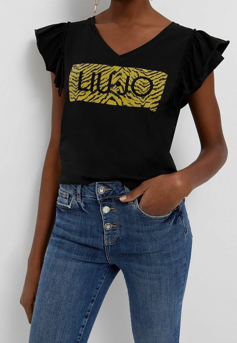 Top nero a maniche corte con dettagli arricciati, caratterizzato da un logo "LIU JO" a righe gialle di tigre su uno sfondo rettangolare.